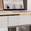 A close-up view of a white desk with a gold trim, showing drawers and a laptop. Produktbild-Vorschau