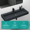 A dark gray rectangular washbasin mounted on a wall, with a black faucet and two bottles of soap or lotion on the right side. Below the washbasin are three teal-colored boxes with icons and text describing product features. Produktbild-Vorschau