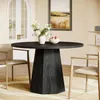 A round dining table with a unique pedestal base is set in a dining room with chairs, a vase of flowers, and fruit. Produktbild-Vorschau