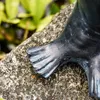 A close-up of a dark-colored statue's flipper resting on a textured stone. Produktbild-Vorschau