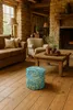 A cozy living room with a stone fireplace, wooden furniture, and a patterned ottoman. Produktbild-Vorschau