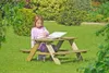 A young girl is sitting at a wooden picnic table in a garden, reading a book. Produktbild-Vorschau