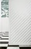 A close-up of a white 3D wall panel with a diagonal pattern, next to a wall with patterned wallpaper and fluted wainscoting, and a black and white checkered floor. Náhľad obrázku produktu