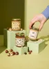 A hand reaching for a jar of nut butter, with other jars and nuts arranged on green blocks. Produktbild-Vorschau