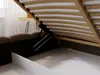Close-up view of the underside of a bed frame with a lifting mechanism, revealing the wooden slats and storage compartment. Produktbild-Vorschau