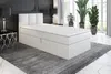 A white boxspring bed with a headboard is shown in a room with a large rug and plants. Produktbild-Vorschau