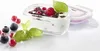 A glass food storage container filled with yogurt and topped with berries and chocolate shavings, with fresh berries and basil leaves scattered around it. Náhled obrázku produktu