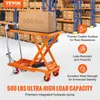 A scissor lift table in a warehouse setting with boxes on shelves in the background. Voir les images du produit
