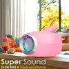 A pink portable stereo radio with LED lighting is placed on a wooden surface in front of a window with autumn trees visible outside. Several colorful children's toys are arranged around the radio. Voir les images du produit