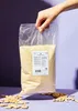 A hand holding a bag of ground almonds with loose almonds scattered around the base. Produktbild-Vorschau
