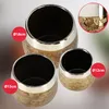 Three ceramic pots of varying sizes are displayed against a gradient background. The pots have a textured gold exterior with a silver band near the rim and a black interior. Red circles with white text indicating diameters are overlaid on the image. Produktbild-Vorschau