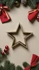 A wooden star is placed on a light beige background, surrounded by Christmas decorations like pine branches, red ornaments, and red fabric bows. Produktbild-Vorschau