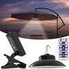 A solar-powered hanging lamp is shown attached to a patio umbrella, with a remote control and a clip-on battery pack also visible. The scene is set against a twilight sky and water. Anteprima dell’immagine prodotto
