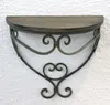 A wall shelf with a wooden top and ornate metal scrollwork base is mounted on a textured white wall. Produktbild-Vorschau