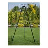 A black metal tripod stand is set up on a green lawn in front of a garden with various plants and trees. Náhled obrázku produktu