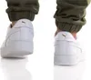 A close-up view of the back of two white Puma sneakers worn by a person, with green pants cuffed above the ankles. Produktbild-Vorschau