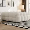 A fluffy beige ottoman-style sofa is placed on a patterned rug in a living room setting. Produktbild-Vorschau