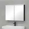 A mirrored medicine cabinet with two doors is mounted on a light gray wall above a white sink with a black faucet. Anteprima dell’immagine prodotto