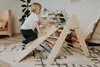 Two children playing on a wooden climbing triangle with a slide indoors. Produktbild-Vorschau