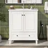 A white bathroom vanity with a ceramic sink is shown in a bathroom with green tiled walls. Náhled obrázku produktu