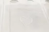 A close-up view of a white net curtain with a heart pattern. Produktbild-Vorschau