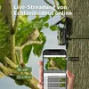 A trail camera mounted on a tree, with a smartphone displaying a live view of the camera's feed, and text overlays highlighting features. Produktbild-Vorschau