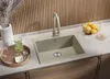 A modern kitchen sink setup with a beige granite sink, a matching faucet, and various accessories like a pitcher of green liquid, glasses, and a bowl of fruit. Produktbild-Vorschau