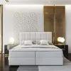 A modern bedroom with a large white boxspring bed as the focal point. Produktbild-Vorschau