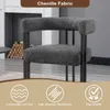 A dark gray chenille armchair with black metal legs is shown in a room with a fireplace and stacked logs in the background. The bottom of the image has three circular icons with text descriptions. Produktbild-Vorschau