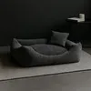 A gray corduroy dog bed with a small pillow is placed on a gray rug in a dimly lit room. Produktbild-Vorschau
