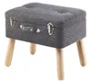 A gray upholstered ottoman with wooden legs, designed to resemble a vintage suitcase.