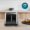 A black and silver toaster sits on a wooden countertop next to a croissant. A blue circular graphic with a speedometer icon is in the upper right corner. Anteprima dell’immagine prodotto