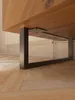 Close-up view of the underside of a wooden furniture piece supported by black metal legs. Produktbild-Vorschau