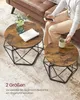 A person is sitting on a sofa next to two round coffee tables. One table has a vase with flowers and a folded towel on it. The other table has a mug on it. The tables have a rustic wood top and a geometric black metal base. Podgląd zdjęcia produktu