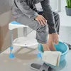 A person is sitting on a shower stool and soaking their feet in a blue basin. Produktbild-Vorschau