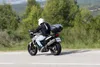A person riding a motorcycle on a road with trees in the background. Podgląd zdjęcia produktu