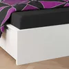 A close-up view of a bed with a black fitted sheet and a duvet cover with a geometric purple and white pattern. Produktbild-Vorschau