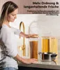 Frau setzt einen Bambusdeckel auf einen hohen klaren Glas-Aufbewahrungsbehälter, gefüllt mit Spaghetti, auf einer Küchenarbeitsplatte Produktbild-Vorschau