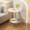 A small round side table with two shelves next to a bed. Produktbild-Vorschau