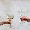 Two hands are holding up two decorative glasses against a textured wall. Produktbild-Vorschau