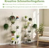 Two white butterfly-shaped plant stands filled with various potted plants, set against a light-colored wall and wooden floor. Produktbild-Vorschau