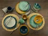 A collection of ceramic dinnerware, including plates, bowls, and mugs, arranged on a wooden surface. Náhľad obrázku produktu
