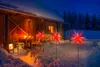 A wooden cabin in the snow at night, decorated with red star-shaped lights. Produktbild-Vorschau