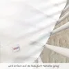 A white sheet or mattress protector is laid out, with a small label visible. The image is taken from a slightly elevated angle, showing the texture of the underlying surface. Produktbild-Vorschau