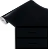 A roll of black contact paper is shown diagonally, partially covering a black drawer unit with two drawers. Produktbild-Vorschau