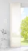 A panel curtain hangs in front of a large window with a view of a green tree and blue sky. A small white side table with a plant is to the left. Produktbild-Vorschau
