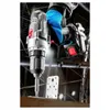 A person wearing gloves is using a cordless drill to attach a metal plate to a wooden surface. Podgląd zdjęcia produktu