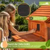 Two people, a woman and a child, are looking at a wooden chicken coop in a garden setting. There are overlays with text and graphics. Produktbild-Vorschau