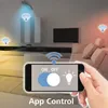 A hand holding a smartphone displaying a smart home app interface, with a living room scene in the background showing smart lights controlled by the app. Produktbild-Vorschau