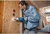 A man is using a Bosch hammer drill to make a hole in a wooden wall. Voir les images du produit